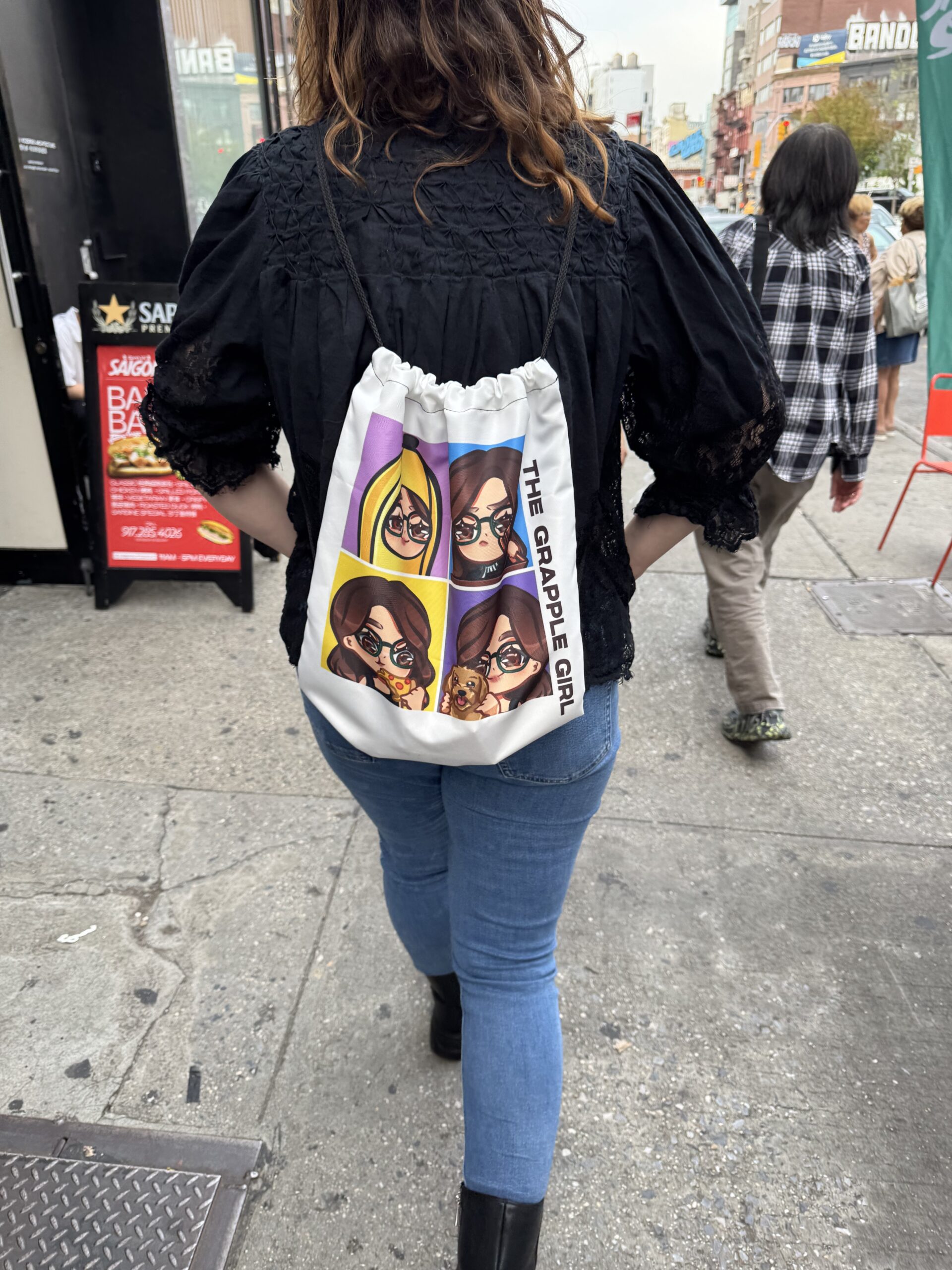 Grapple walking in the street of NYC with "thegrapplegirl" backpack showing 4 emotes: Grapple as a banana, Grapple as a judge, Grapple eating pizza, and Grapple with her dog, West.